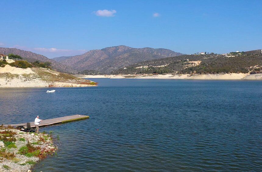 The Germasogeia Dam reservoir seen from the shore, with a jetty and green hills